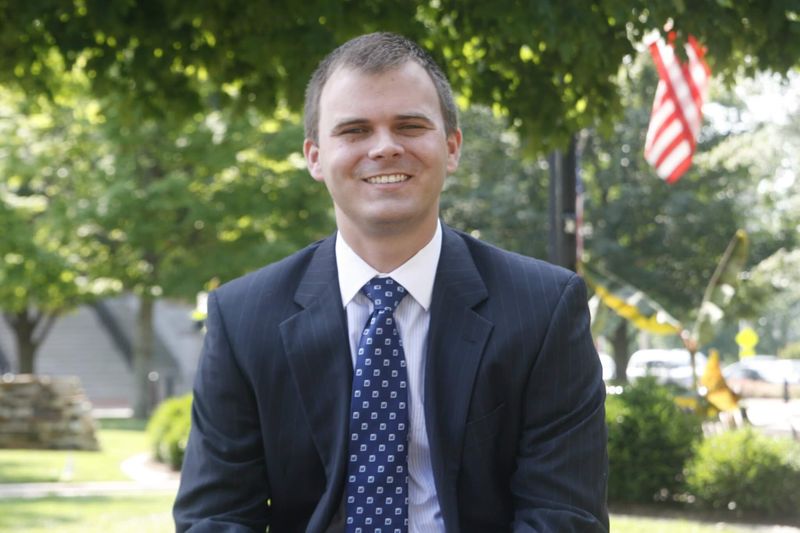 Garrett Ham photographed at the Bentonville town square shortly after the Ouachita feature — in suit and tie with an American flag flying behind him.