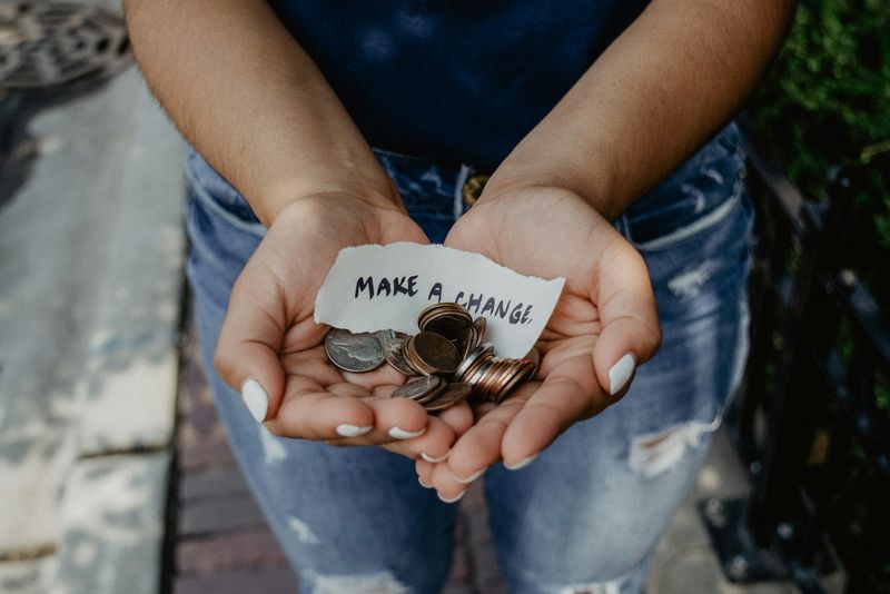 Hands holding coins with a torn paper note that reads "make a change"