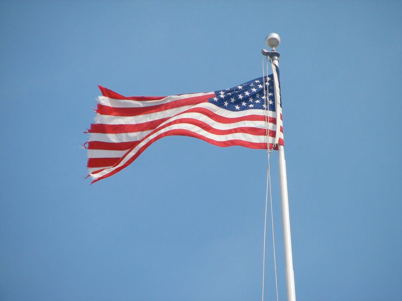 A weather-tattered American flag waving against a clear blue sky