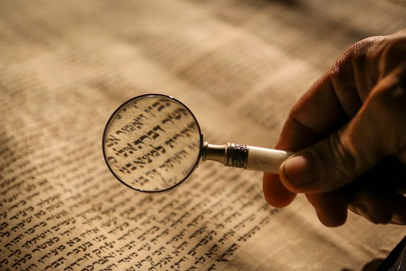 A person examining a historic Old Testament scroll with a magnifying glass