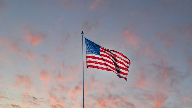 An American flag waving on a flagpole against a cloudy sunset sky