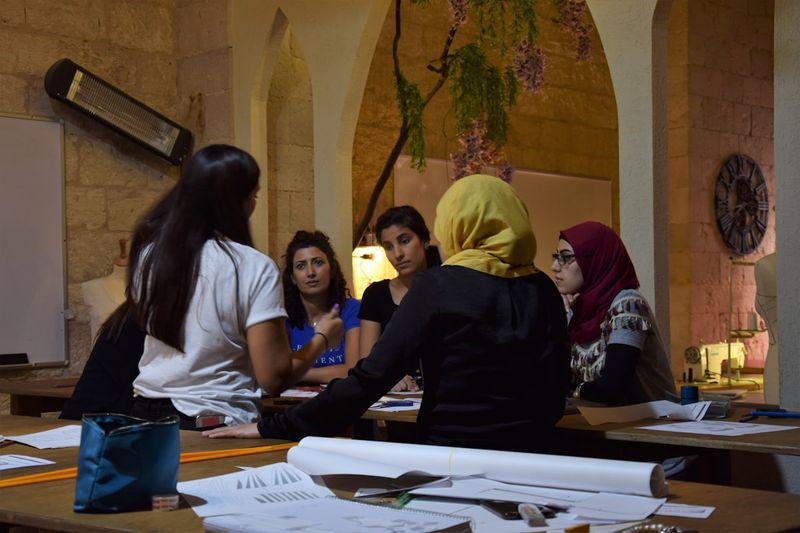 A diverse group of women engaged in discussion around a seminar table in an institutional setting, representing academic discourse and intellectual engagement.